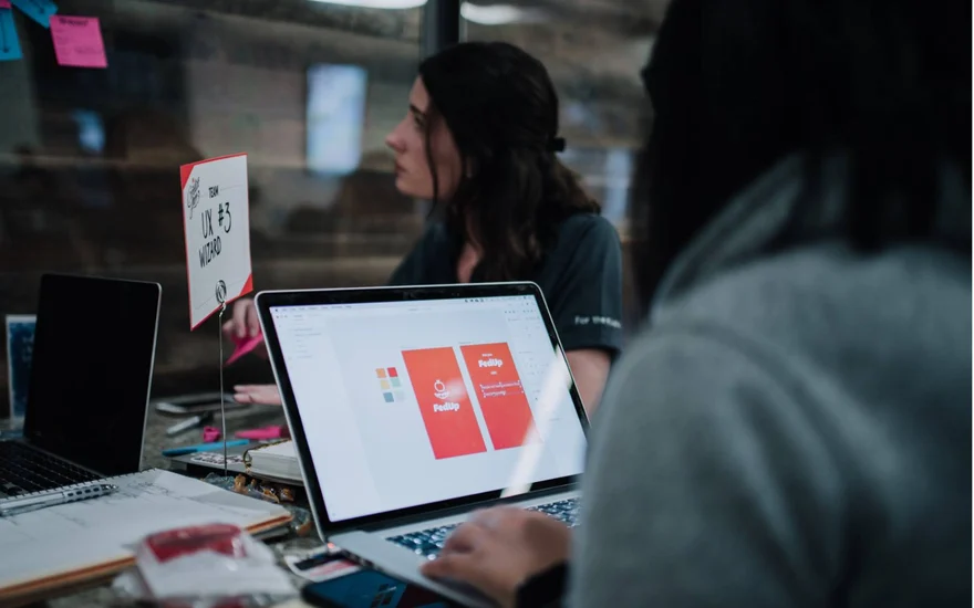The team designing the FedUp screens on a laptop, with the team sign UX #3 Wizard on the table.
