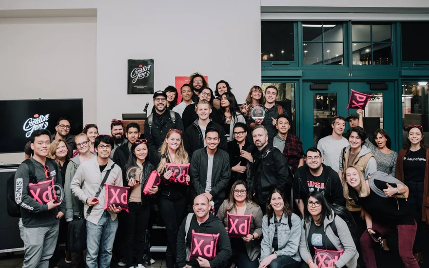 Group photo of the Creative Jam participants and mentors with trophies and Adobe XD pillows.