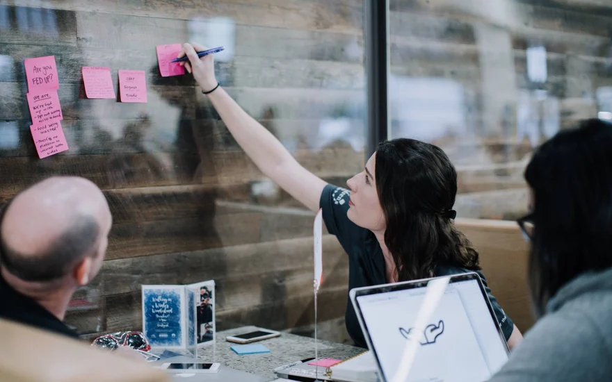 A teammate adds a sticky note to the wall during the Creative Jam; notes read Are you fed up? and list the problems the team chose.